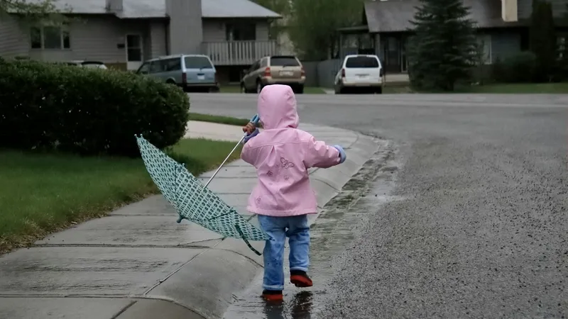 Dziecko w różowej kurtce z parasolem na mokrym chodniku w deszczowy dzień