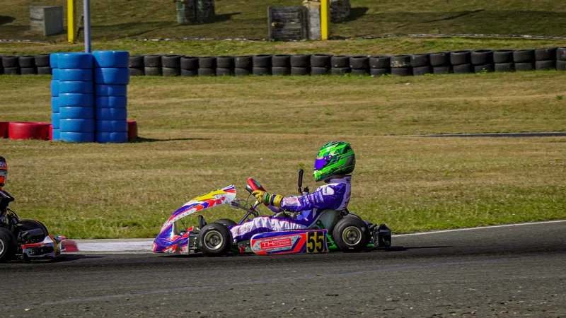 Młody kierowca w kasku i kombinezonie prowadzi gokart na torze