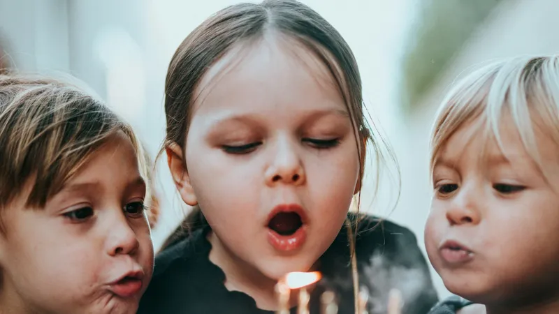 Troje dzieci dmucha w świeczki na urodzinowym torcie