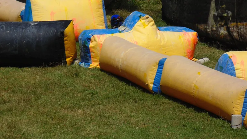 Kolorowe dmuchane przeszkody na trawiastym polu do paintballa, poplamione farbą z kulek
