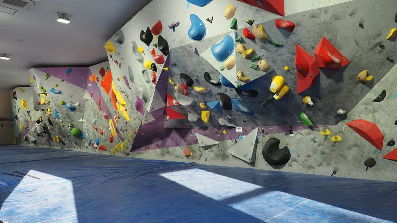 Ściana do boulderingu z kolorowymi chwytami nad niebieskimi materacami w hali wspinaczkowej
